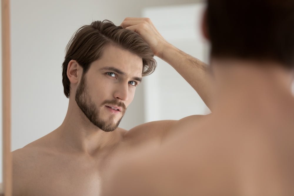 man looking into mirror at his new hair transplant wanting to protect and care for his investment