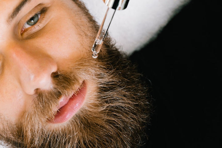 bearded man applies hairmetto face for him oil from a dropper to his moustache